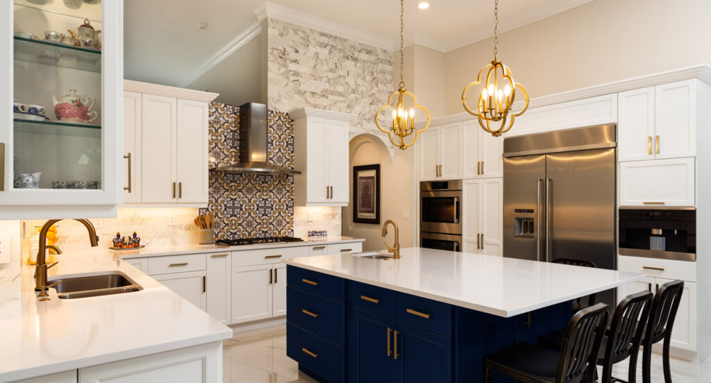 Modern kitchen with white cabinets, a blue island, gold fixtures, stainless steel appliances, and decorative tile backsplash. Two pendant lights hang over the island.
