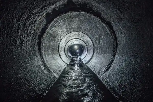 View of a dimly lit, circular underground tunnel with flowing water along the bottom.
