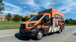 Orange And Black Mcquillan Bros Service Van Driving On A Road, With Company Logo And Website On The Side.