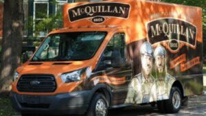 Orange And Black Mcquillan Bros. Service Van Parked On A Street, Featuring Illustrated Workers On Its Side.