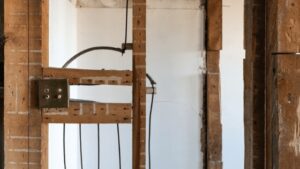 Wooden Beams And Metal Bars Are Exposed In A Partially Constructed Or Renovated Wall, With Electrical Wires Visible.