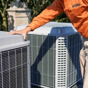 Person In An Orange Shirt Inspecting Two Large Outdoor Air Conditioning Units On A Rooftop.