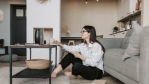 A Woman Sits On The Floor By A Sofa, Using A Tablet And Stylus At A Low Table In A Modern Living Room.
