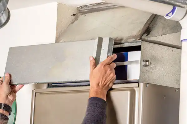 Hands Are Carefully Removing A Metal Cover From An Hvac Unit, Revealing The Intricate Interior Components, As Part Of Routine Furnace Maintenance.