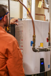 Mcquillan Technician In Orange Shirt Inspecting A Tankless Unit During A Water Heater Replacement Or Installation Service.