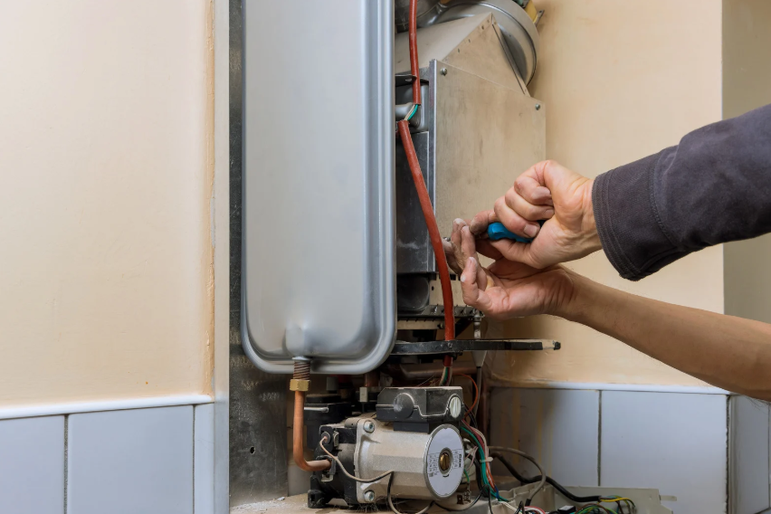 A Person Uses A Screwdriver To Repair Or Maintain An Open Gas Boiler Mounted On A Wall.