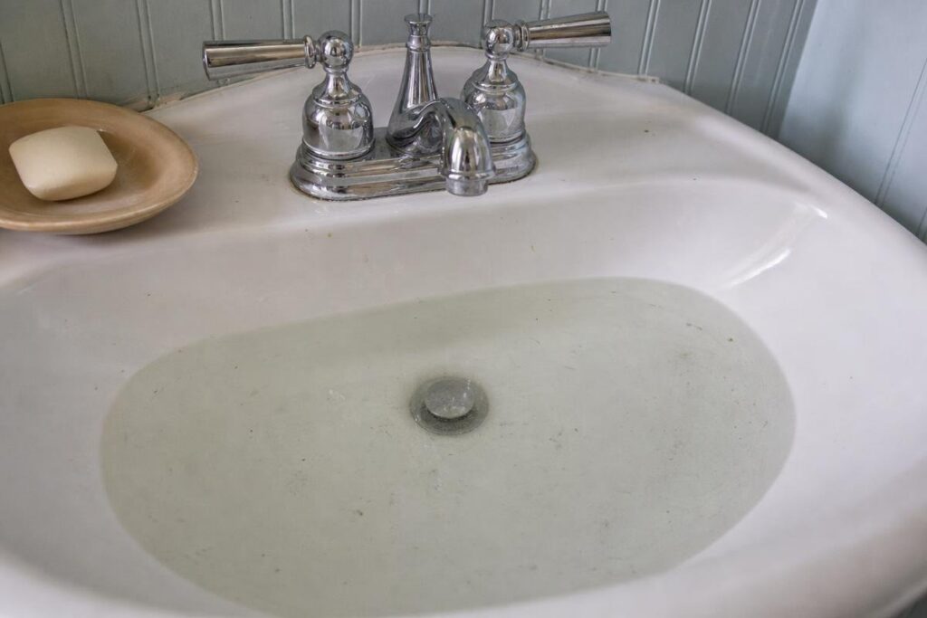 A White Sink Filled With Water, With A Chrome Faucet And A Soap Bar On A Dish To The Left Side, Hints At The Possible Effects Of Low Water Pressure In House Settings.