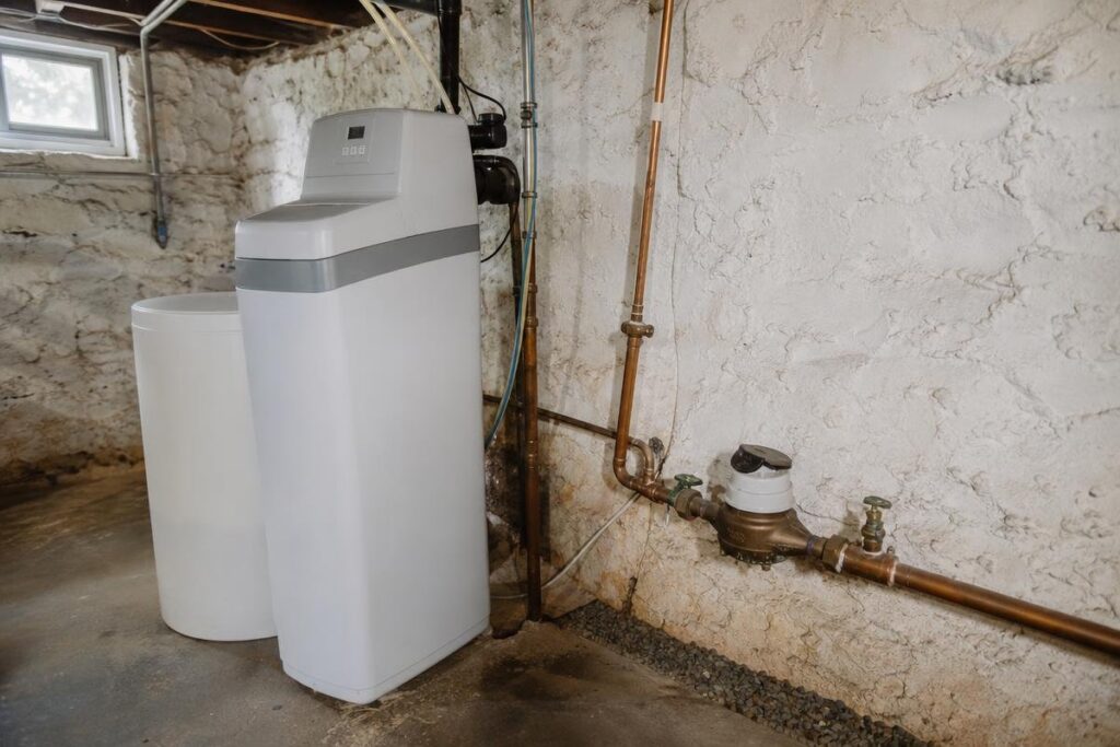 A water softener system installed in a basement with exposed pipes and a concrete floor can help alleviate issues like low water pressure in the house by preventing mineral buildup in your plumbing.