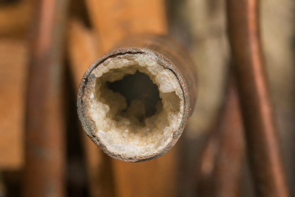 Close-Up Of A Corroded Metal Pipe With Heavy White Mineral Buildup Blocking Most Of The Interior, A Common Cause Of Low Water Pressure In House Plumbing.